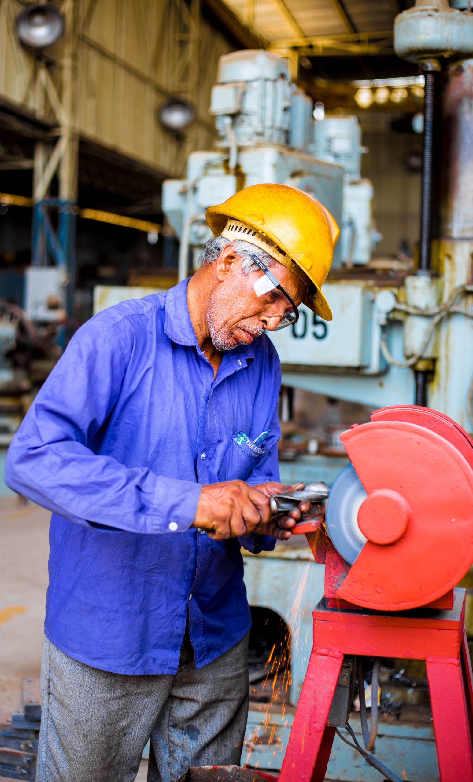 An older man with a hard hat using a benchtop wheel grinder in a workshop.