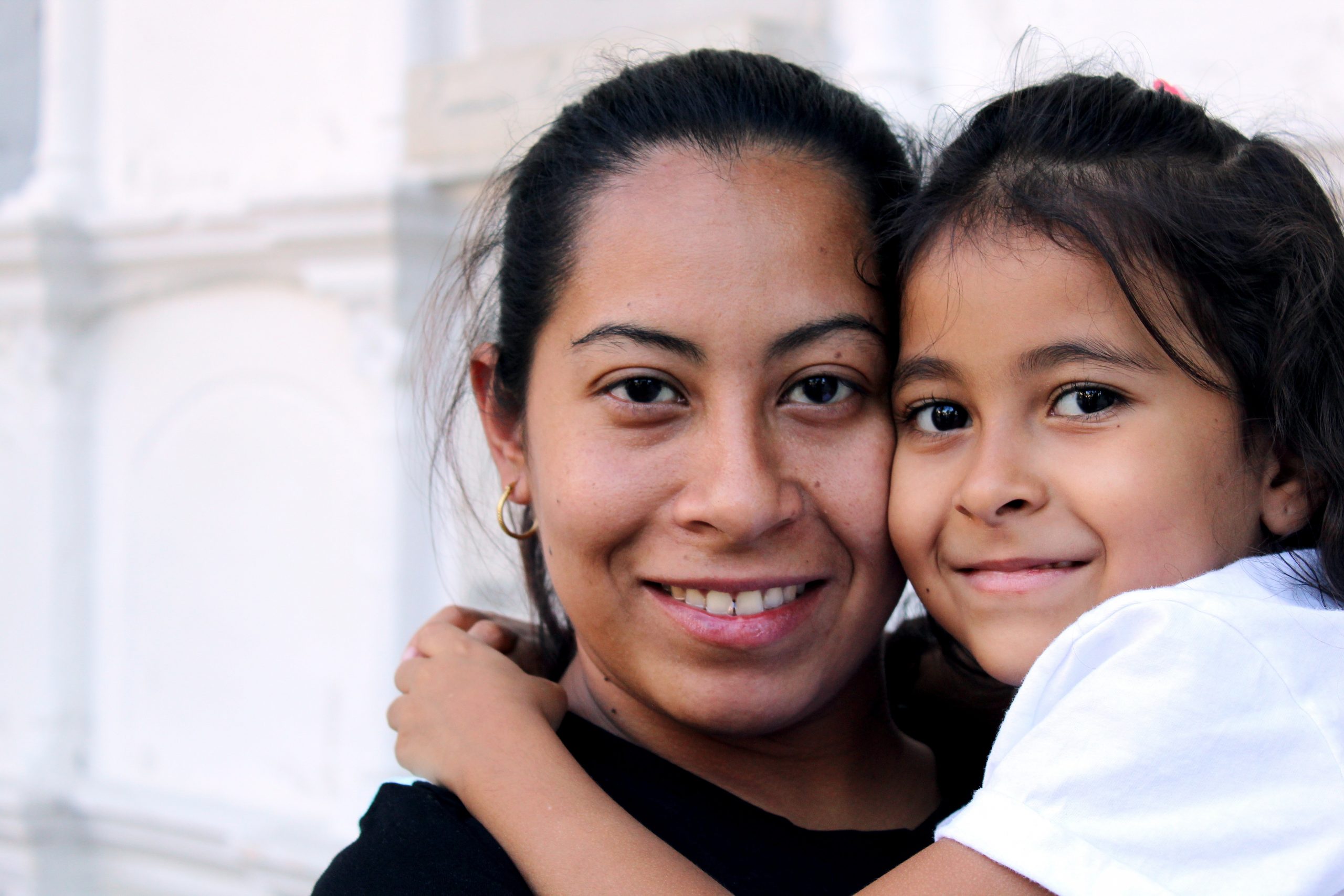 An up close photograph of a columbian mother and daughter hugging and smiling.