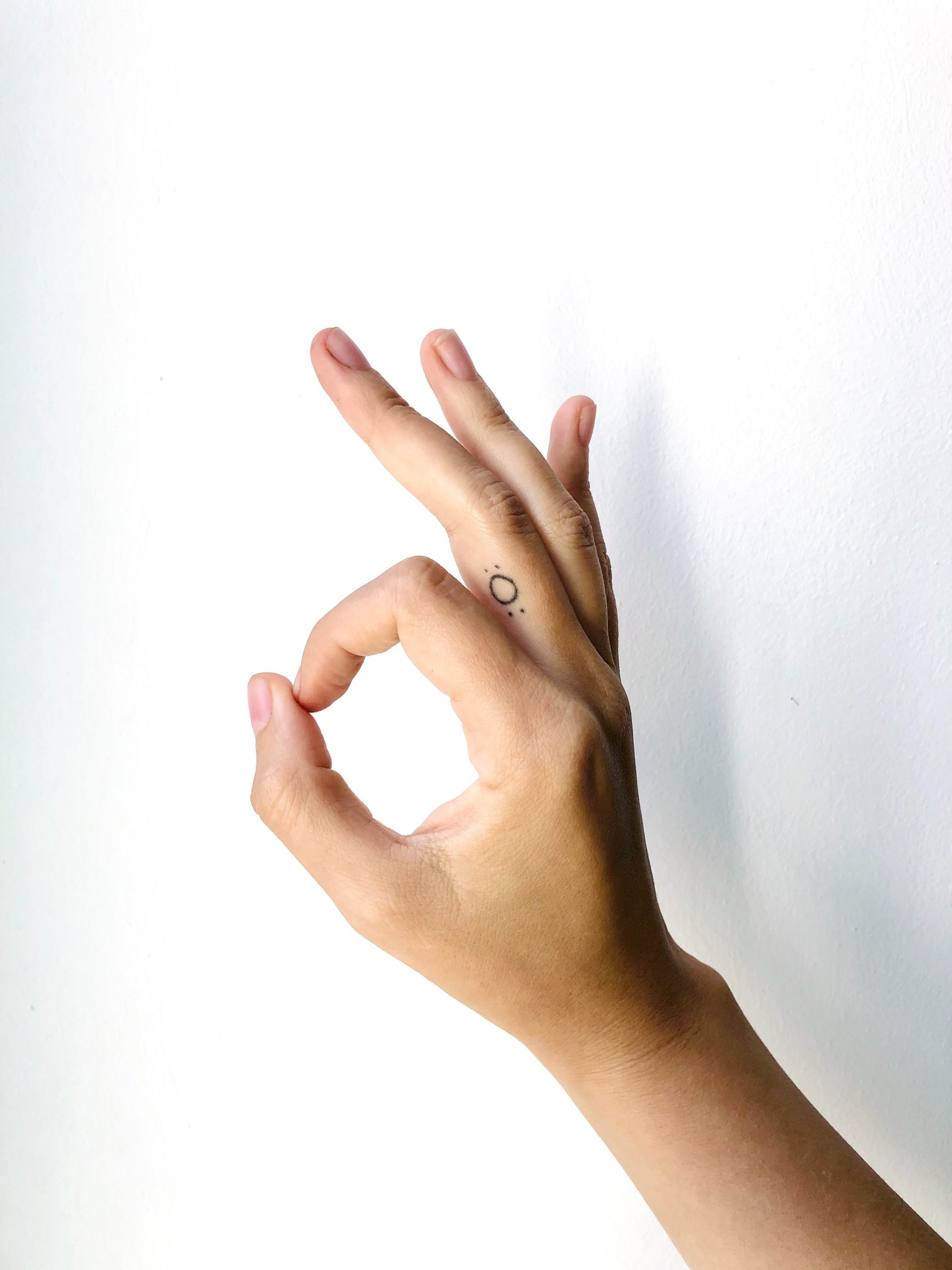 Photograph of a hand against a white background holding the OK hand sign.