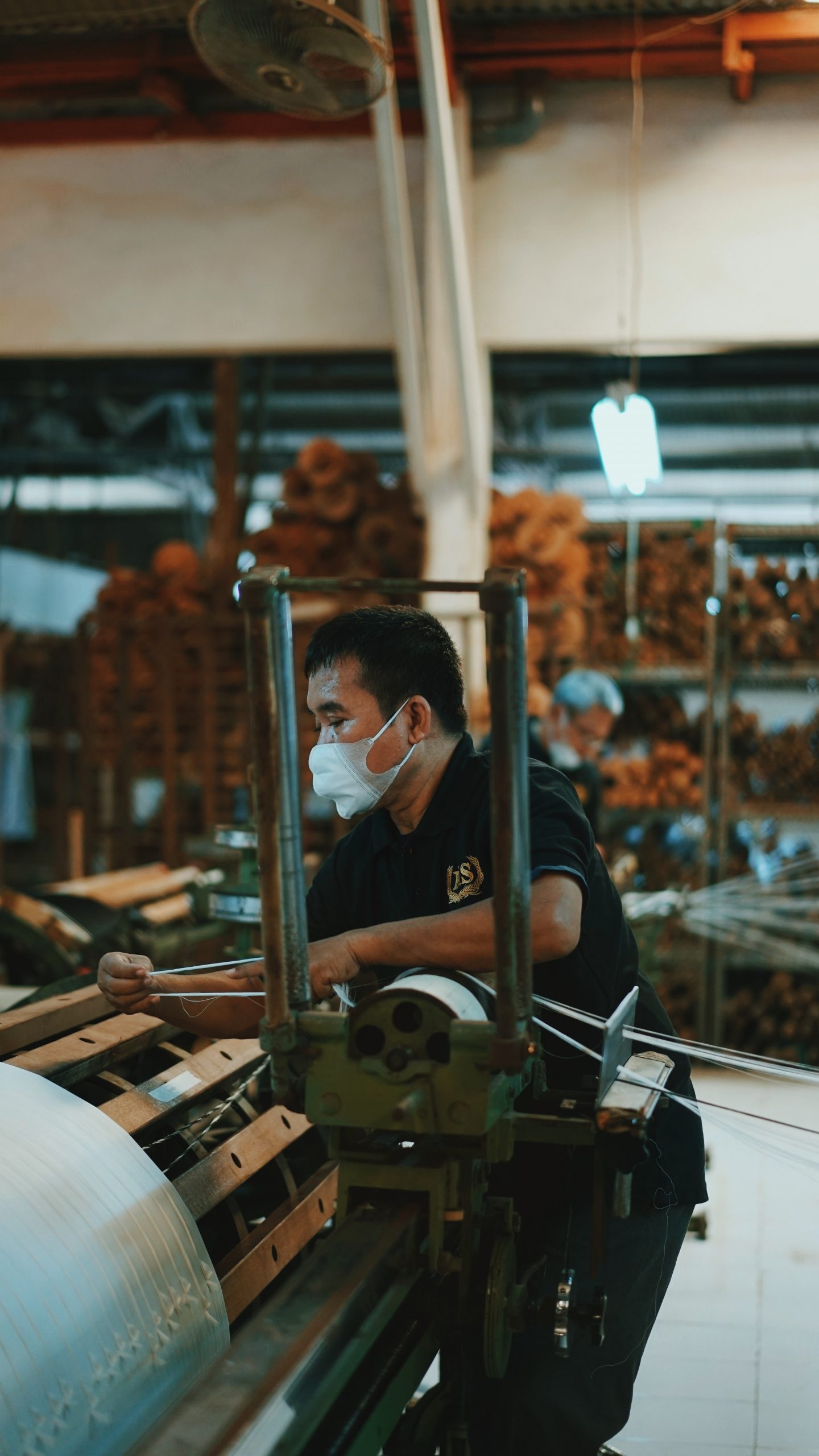 An older man with a mask on using machinery in a workshop.