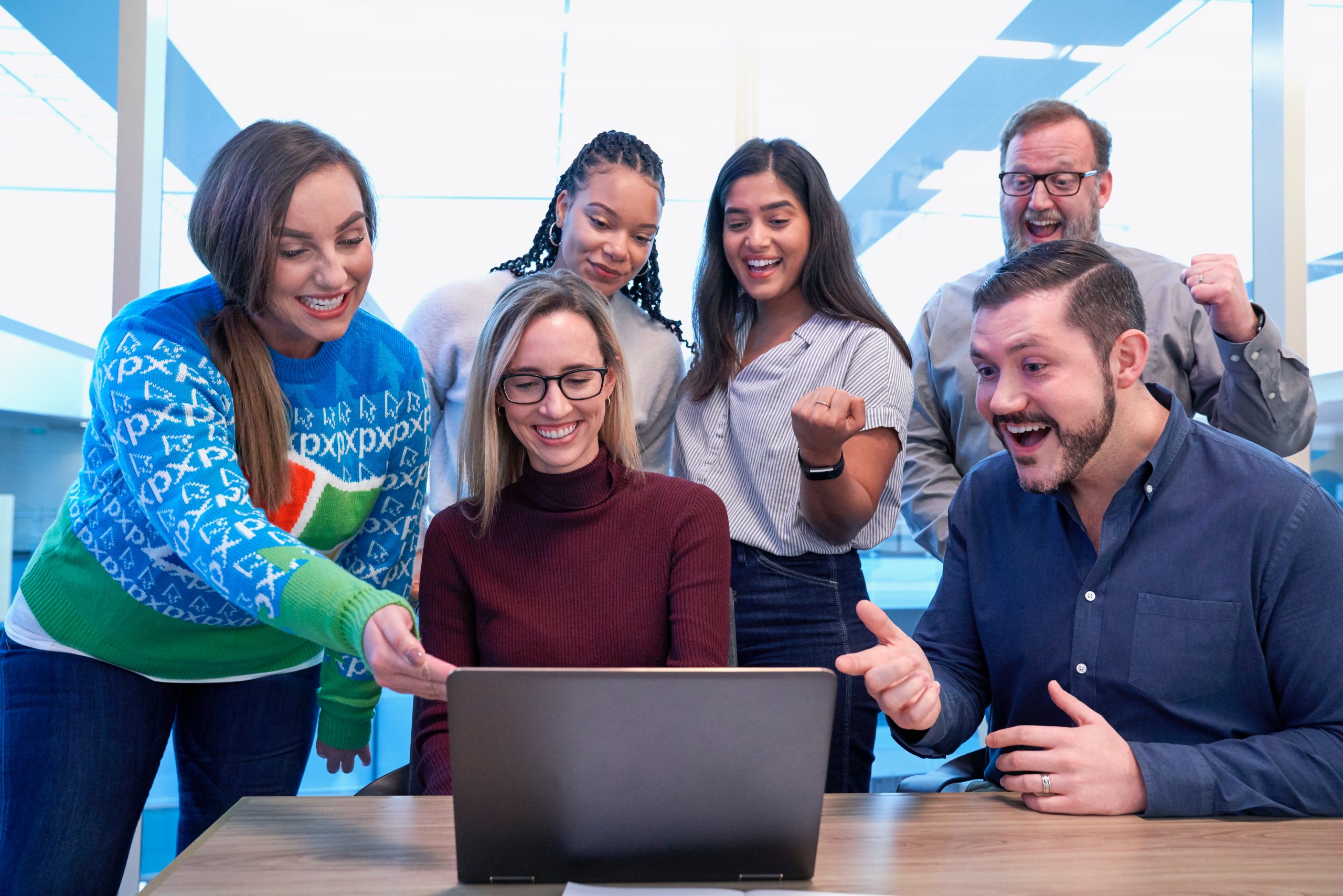 A group of 6 smiling, fist pumping, and pointing at a computer screen.