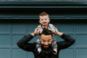 A parent with their child on the shoulders. Both are smiling.