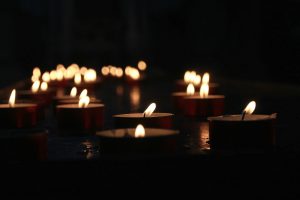 Lit tea light candles in the dark, extending into the distance. Candles in middle are in focus while those at other distances are blurred.